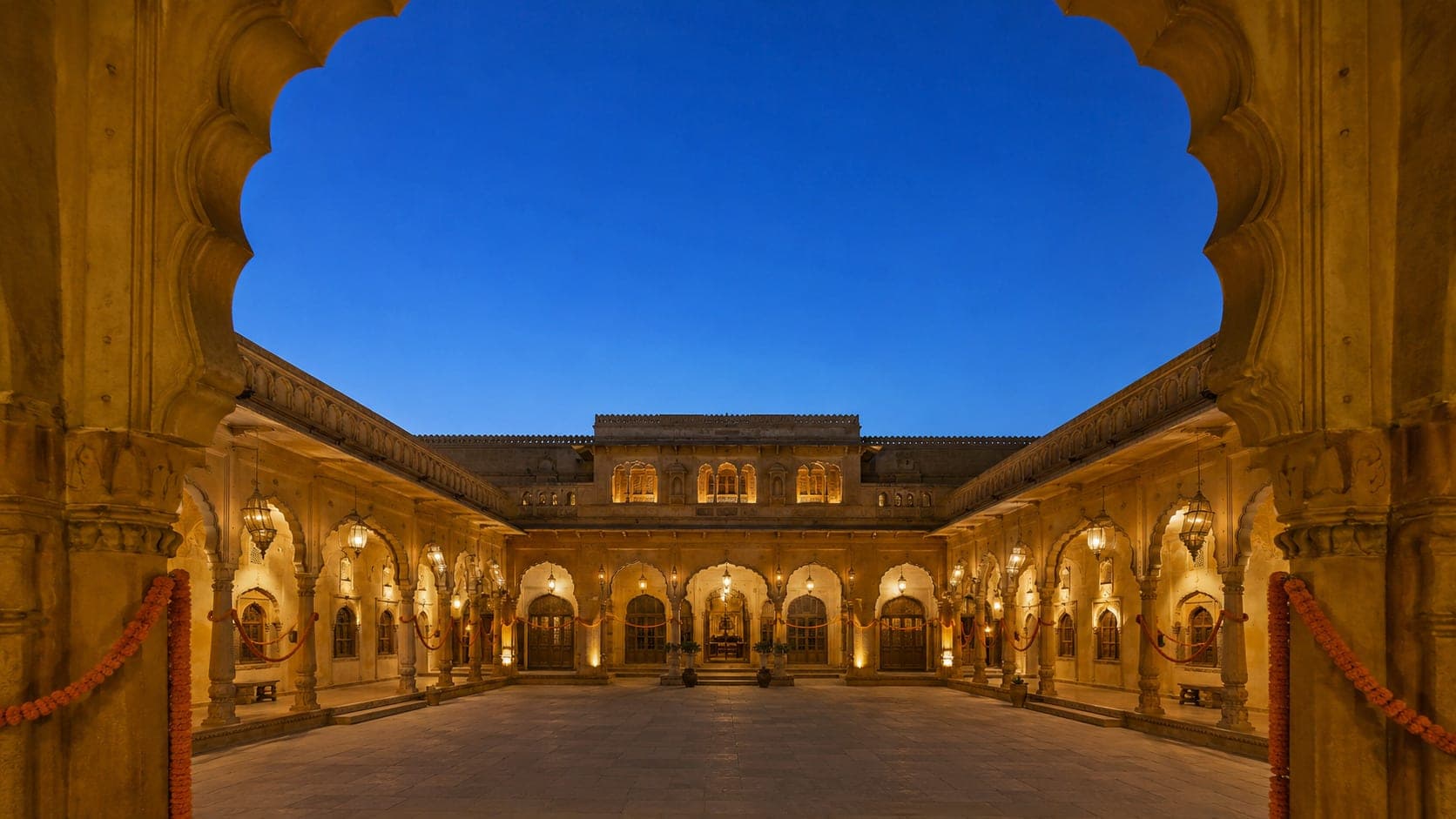 The arched sandstone courtyard of Suryavansh Courtyard at dusk, lit by hanging lanterns